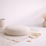 A minimalist meditation setup with a neutral-toned cushion, mala beads, and soft natural light, representing stillness, silence, and introspection.